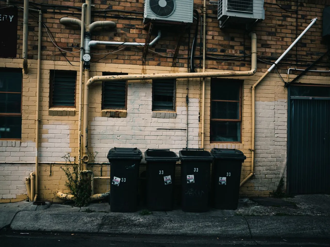 Four garbage bins beneath pipes and air-conditioning units