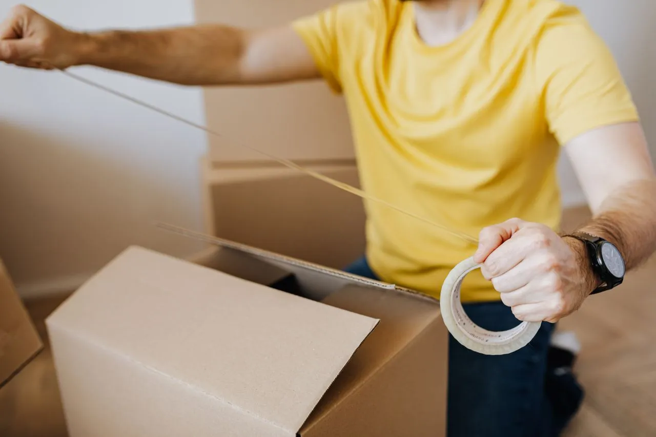 Person sealing a cardboard box with packing tape